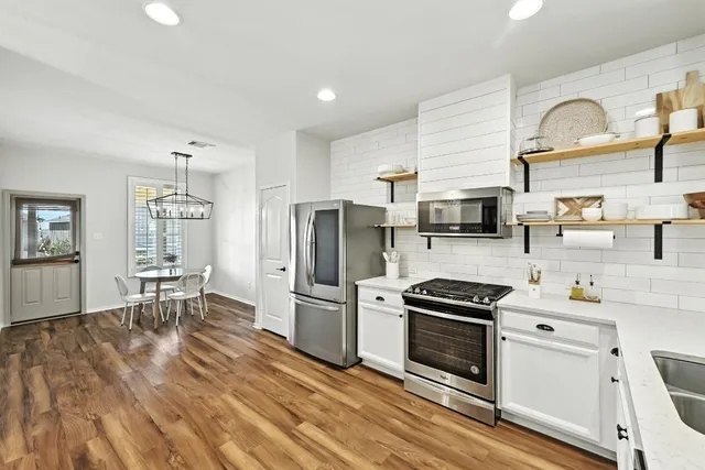 a kitchen with stainless steel appliances a stove a sink a refrigerator white cabinets and wooden floor