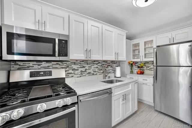 a white kitchen with stainless steel appliances a stove a microwave and a refrigerator