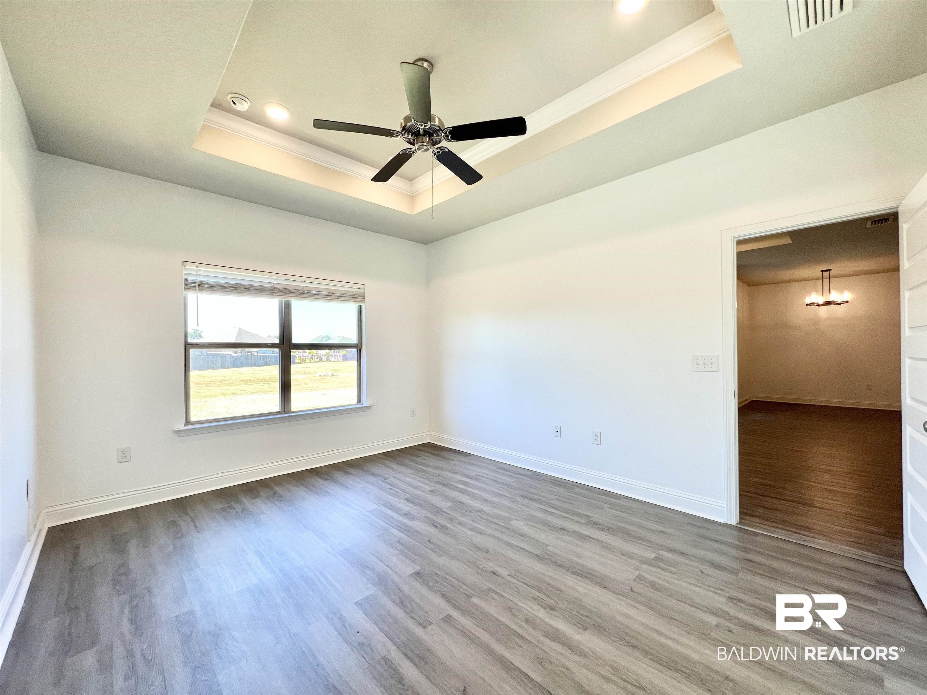 24785 Slater Mill Road Daphne, AL 36526 - Photo 27 of 46 Empty room featuring crown molding, a raised ceiling, wood-type flooring, and ceiling fan with notable chandelier