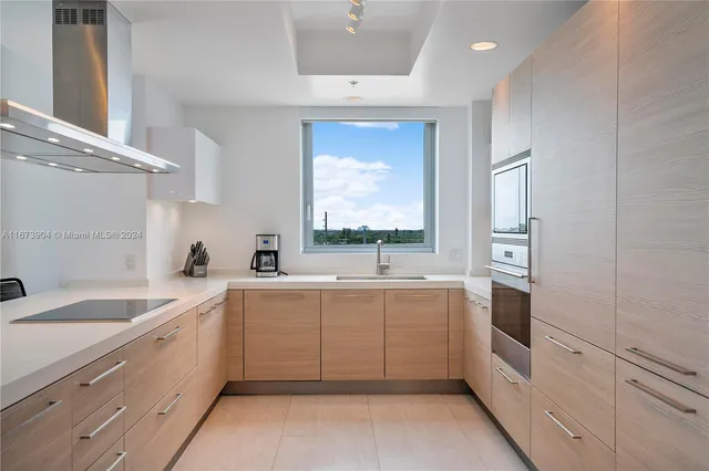 a large white kitchen with a sink a window and stainless steel appliances