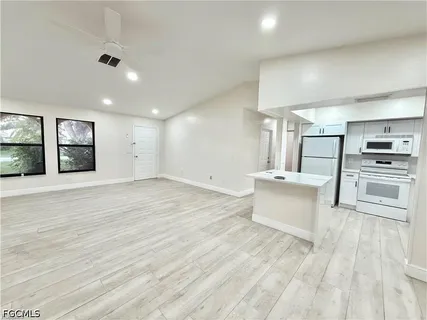 a large white kitchen with kitchen island a stove a sink dishwasher and a refrigerator with wooden floor