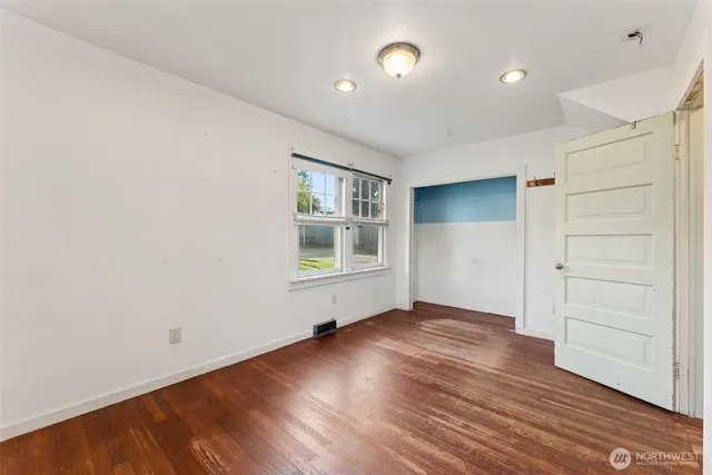 an empty room with wooden floor closet and windows