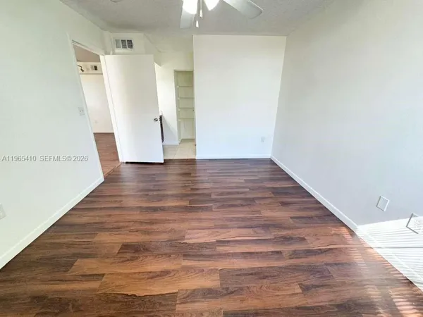 a view of an empty room with wooden floor and a ceiling fan