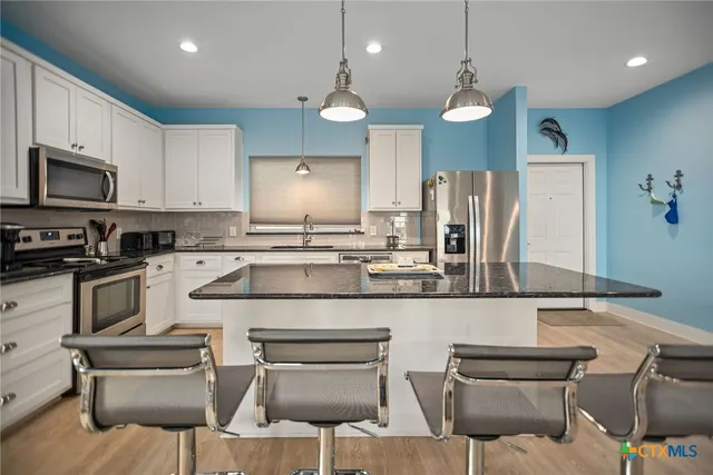 a kitchen with stainless steel appliances granite countertop a sink a stove a refrigerator cabinets and chairs