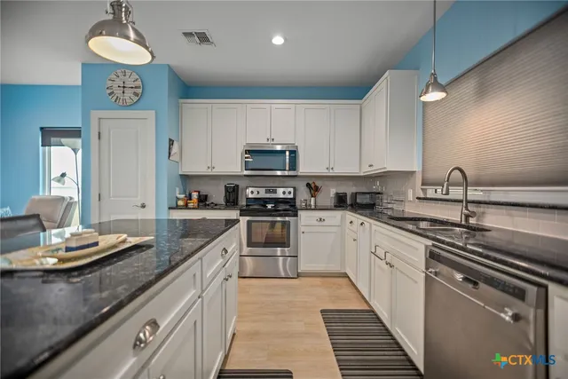 a kitchen with kitchen island granite countertop stainless steel appliances a sink dishwasher a stove a microwave oven and cabinets