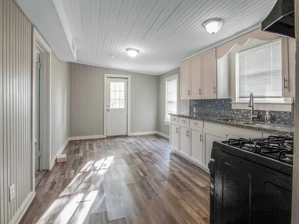 a kitchen with granite countertop a stove a sink wooden floor and cabinets