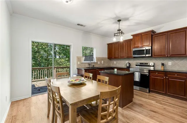 a kitchen with stainless steel appliances granite countertop a kitchen island a stove a refrigerator a sink a dining table and chairs with wooden floor