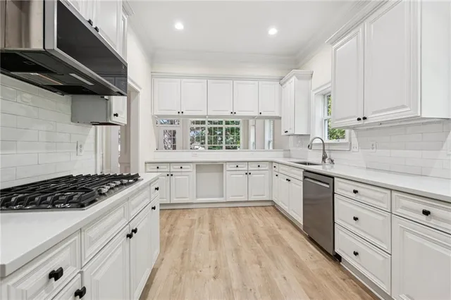 a large white kitchen with stainless steel appliances granite countertop a stove a sink dishwasher and white cabinets with wooden floor