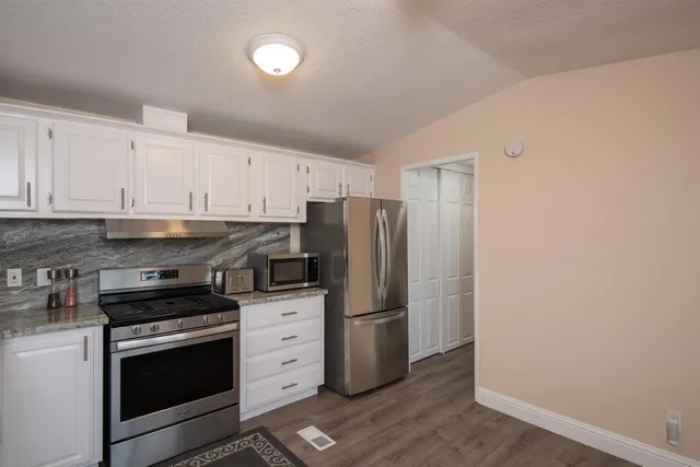a kitchen with granite countertop a refrigerator stove and white cabinets