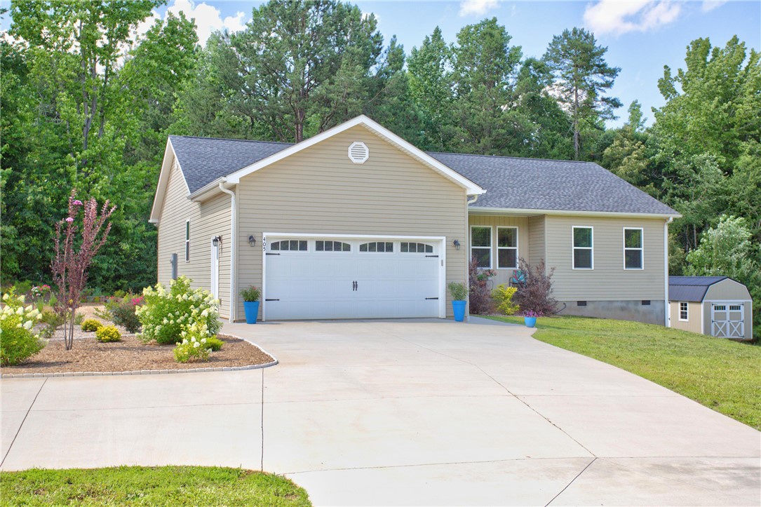 405 Pawnee Drive Walhalla, SC 29691 - Photo 28 of 36 A tan-sided home with an attached garage features a concrete driveway and lush, mature landscaping.