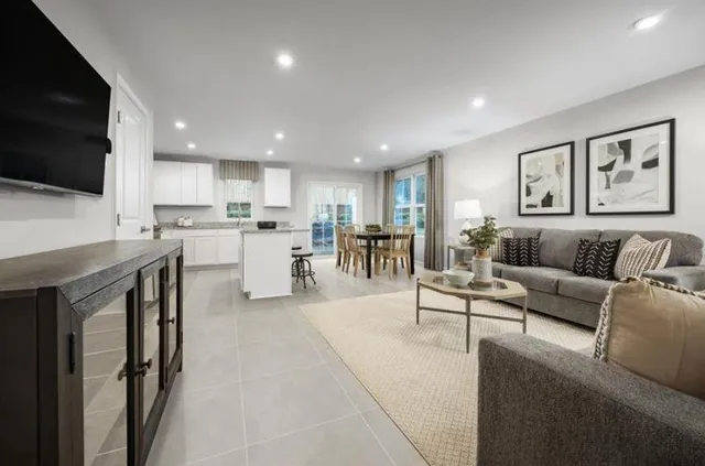 a living room with stainless steel appliances furniture a flat screen tv and kitchen view