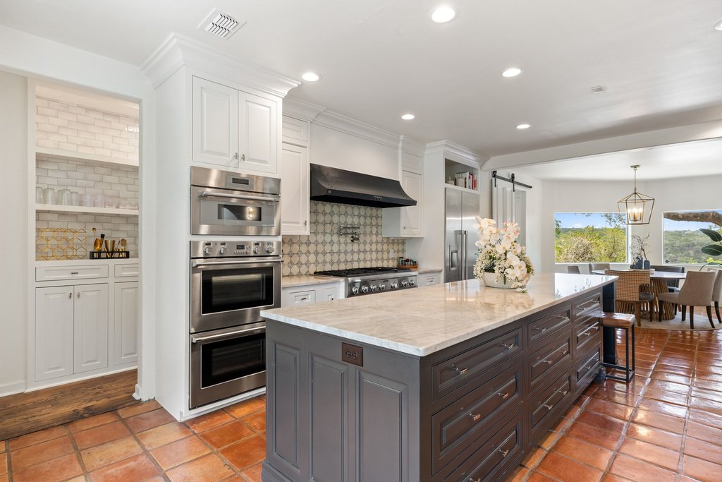 716 North Commons Ford Road Austin, TX 78733 - Photo 5 of 30 Spacious kitchen featuring a large central island with a light-toned countertop, stainless steel double ovens, a built-in refrigerator, a black range hood, and terracotta tile flooring