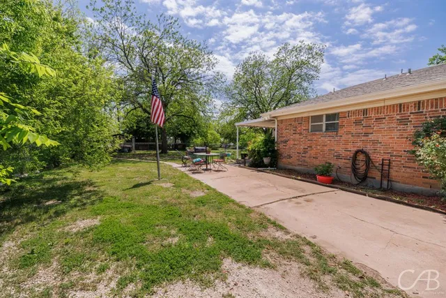 a view of a backyard with table and chairs potted plants and a large tree