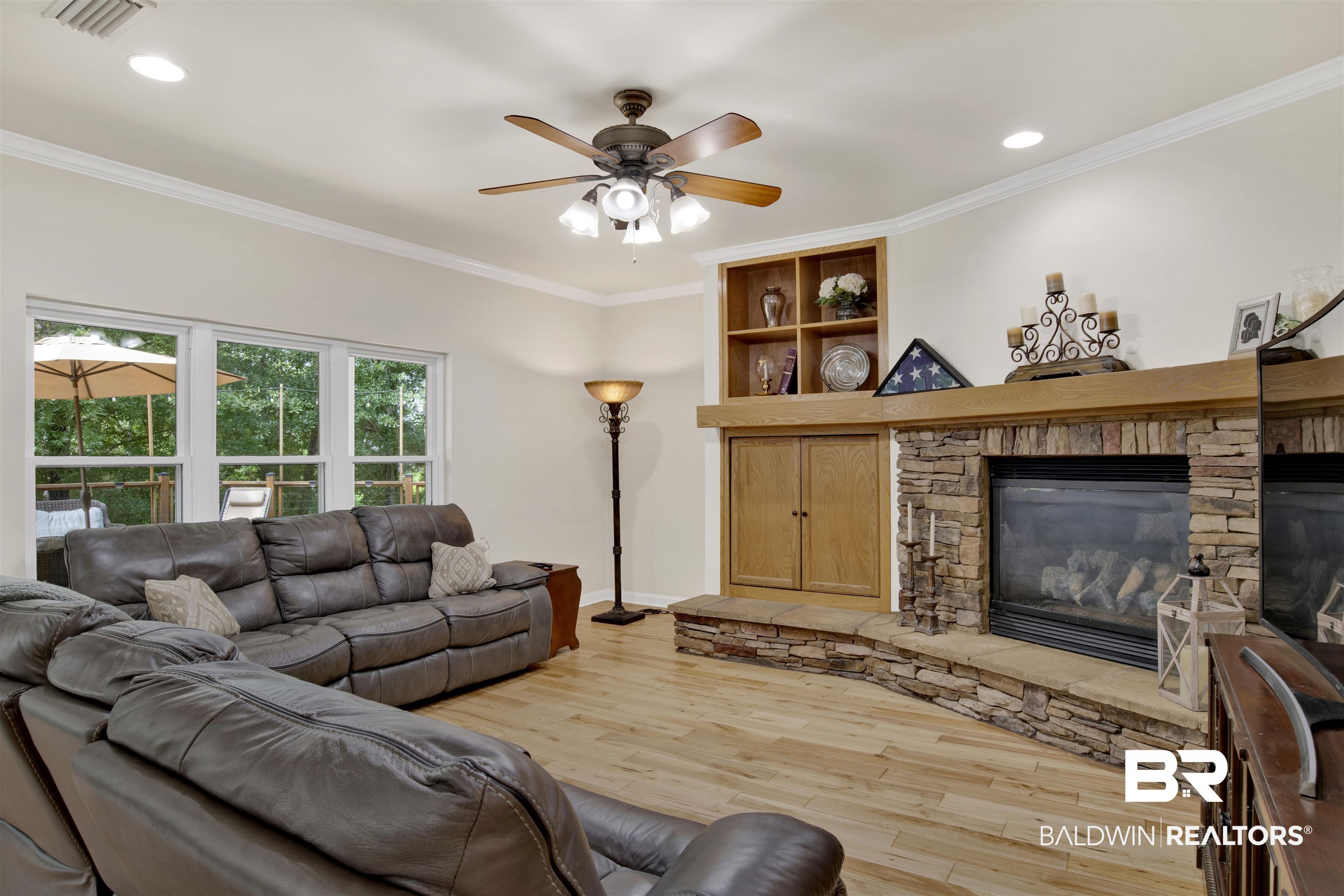638 Southern Way Daphne, AL 36527 - Photo 4 of 26 Living room featuring a stone fireplace, crown molding, light wood-type flooring, and ceiling fan