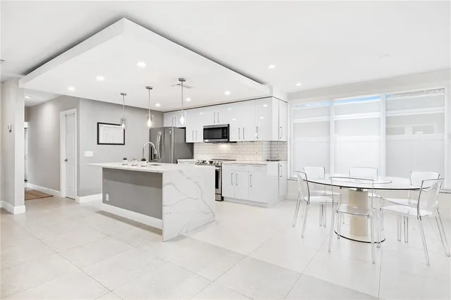 a large white kitchen with kitchen island a large counter top space a sink stainless steel appliances and cabinets
