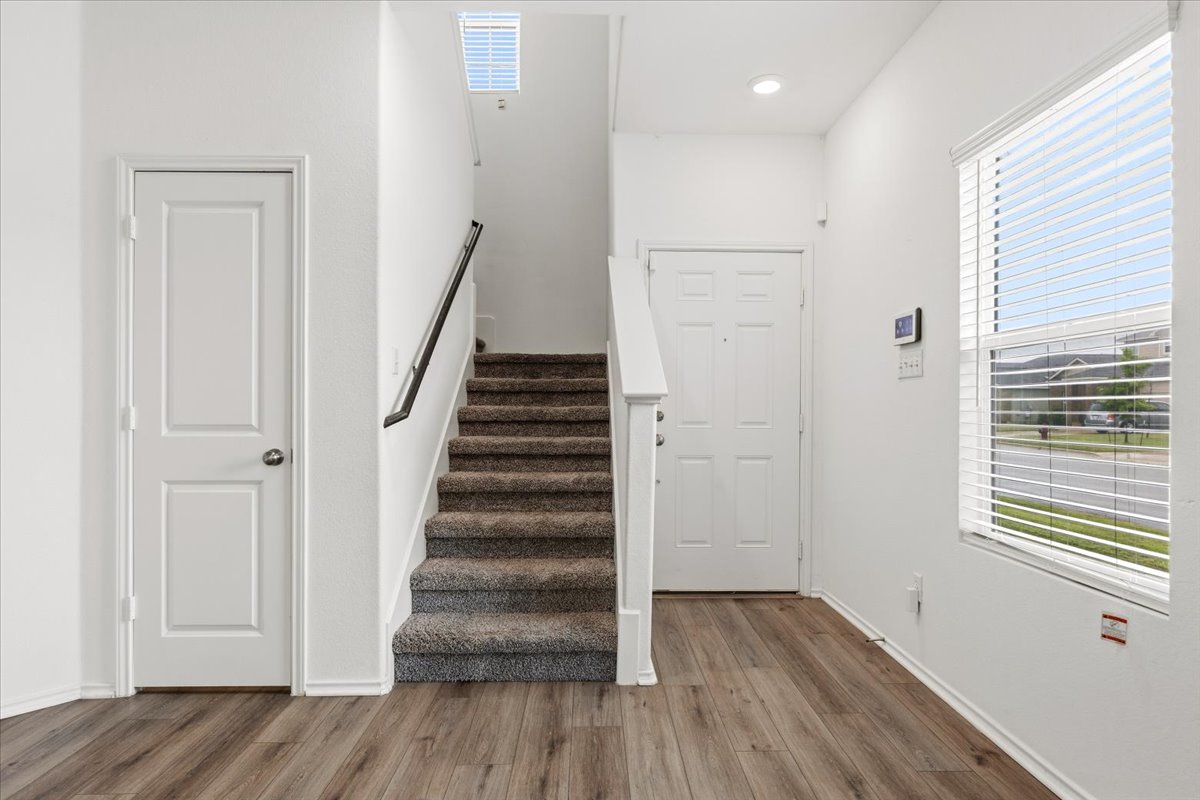 101 Rowdy Yates Way Jarrell, TX 76537 - Photo 5 of 32 Entryway featuring wood-finish flooring, a carpeted staircase with white risers and dark handrail, a skylight, and a large window with horizontal blinds