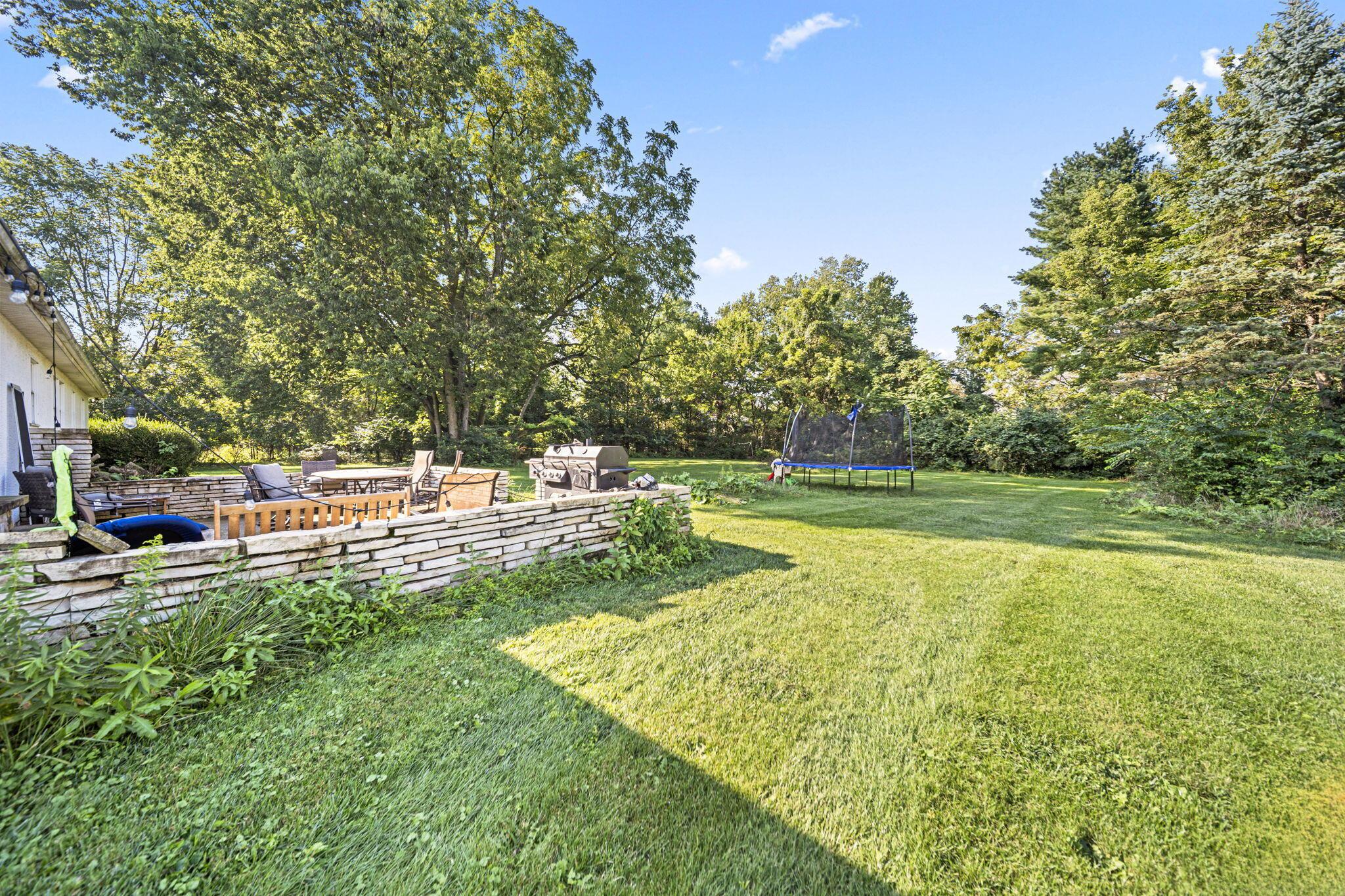 6344 Post Road Dublin, OH 43017 - Photo 28 of 45 Expansive backyard featuring a large grass area, mature trees, a stone retaining wall, and a paved patio area
