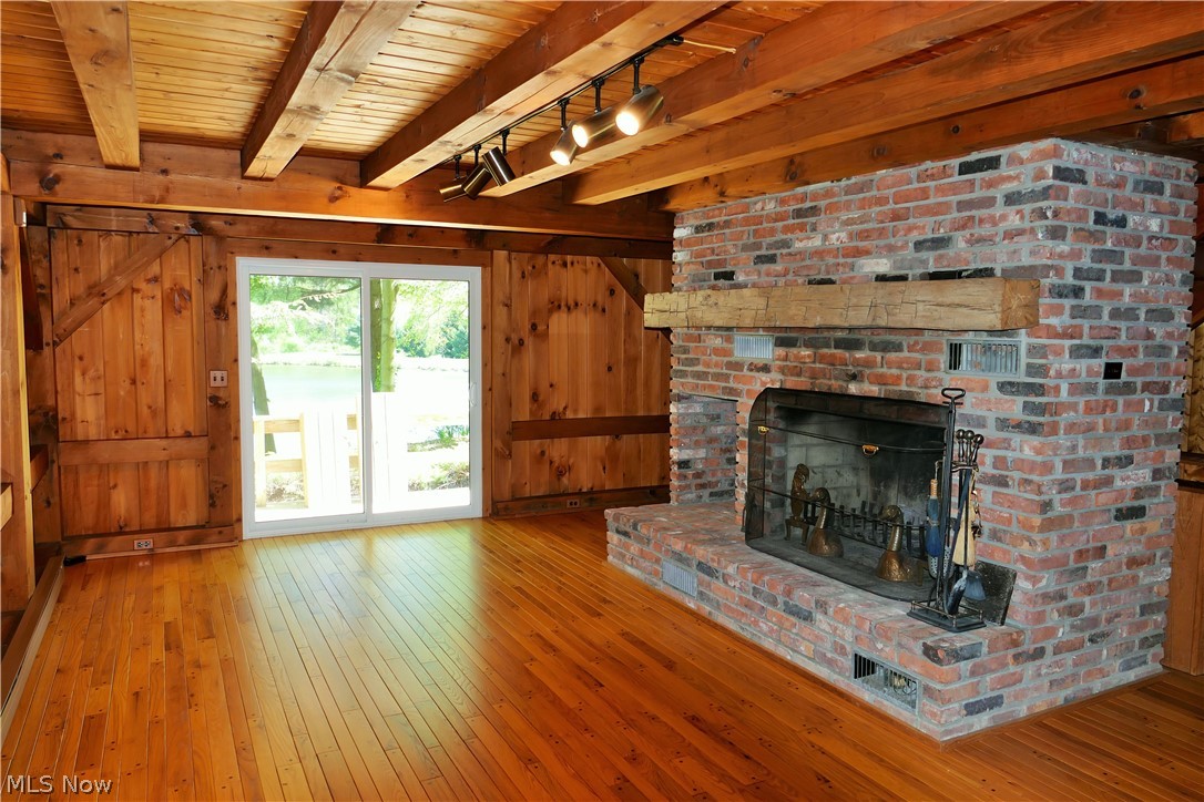 17340 Huntley Road Huntsburg, OH 44046 - Photo 12 of 24 Unfurnished living room featuring a brick fireplace, beamed ceiling, wooden walls, wooden ceiling, and hardwood / wood-style floors
