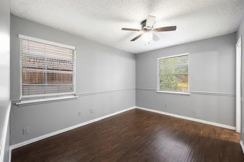 an empty room with wooden floor fan and windows