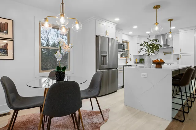 a kitchen with stainless steel appliances kitchen island granite countertop a dining table chairs and a refrigerator