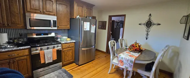 a kitchen with stainless steel appliances granite countertop a refrigerator a stove top oven a sink dishwasher and a dining table with wooden floor