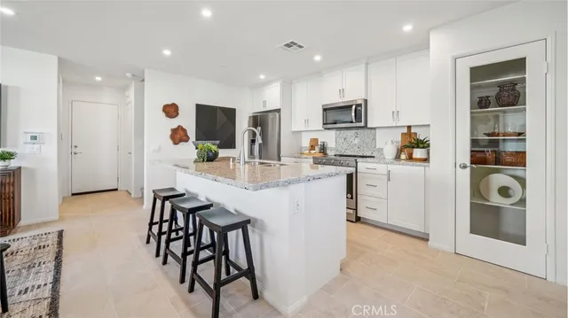 a kitchen with stainless steel appliances granite countertop a stove top oven a sink a refrigerator and white cabinets with wooden floor