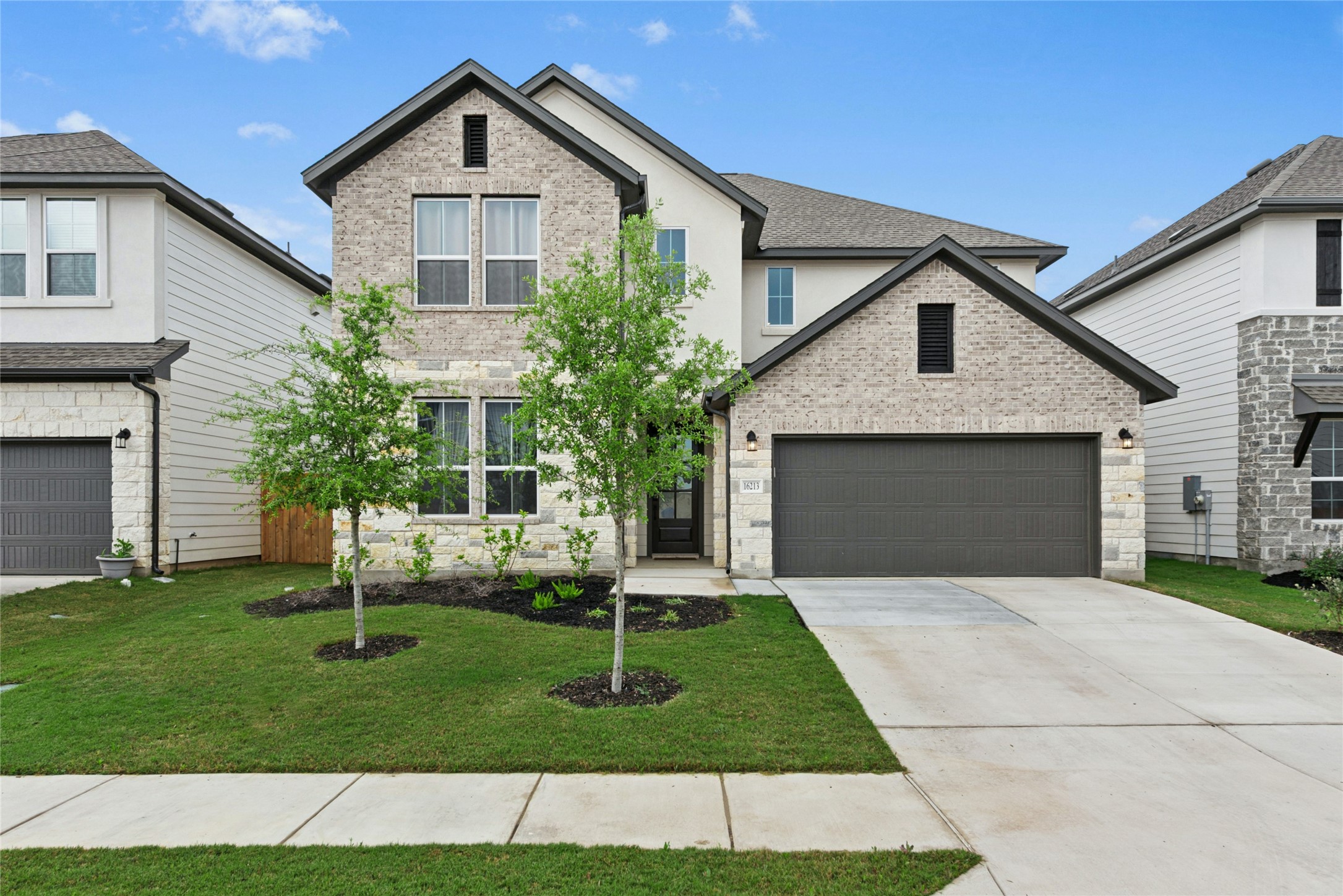 Traditional-style house with driveway, a front lawn, brick siding, and an attached garage