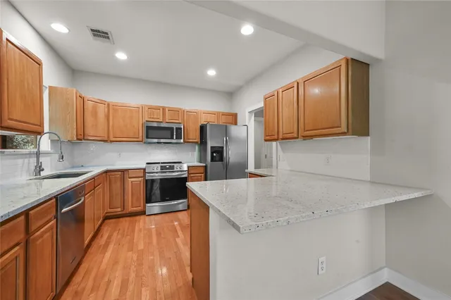 a kitchen with stainless steel appliances granite countertop wooden cabinets a stove top oven a sink and dishwasher with wooden floor