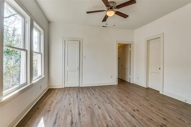 an empty room with wooden floor fan and windows