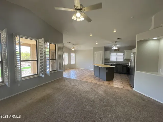 a view of an empty room and kitchen with ceiling fan