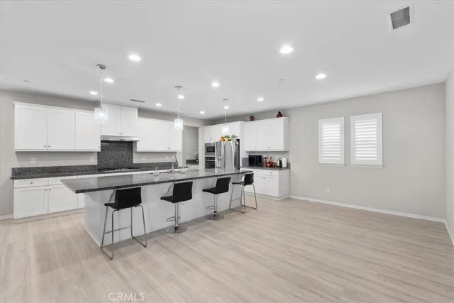 a open kitchen with stainless steel appliances granite countertop a stove a sink a refrigerator and white cabinets with wooden floor