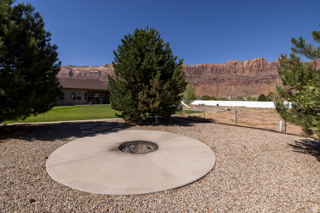 4635 East Sunny Acres Lane Moab, UT 84532 - Photo 27 of 56 Expansive outdoor space featuring a built-in circular fire pit on a gravel base, mature evergreens, and a manicured lawn