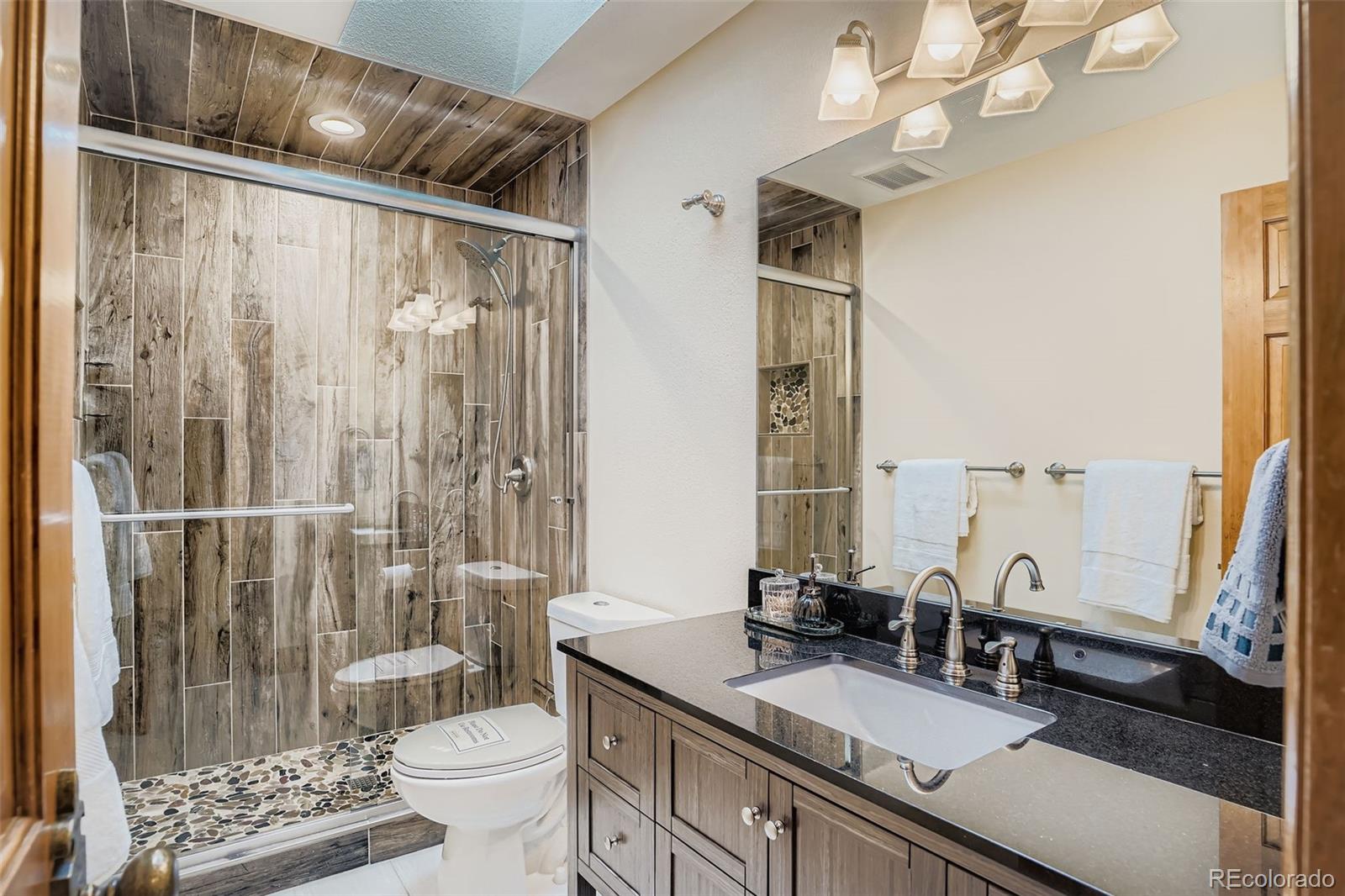 13342 Douglass Ranch Drive Pine, CO 80470 - Photo 20 of 31 a bathroom with a granite countertop sink a toilet a mirror and shower