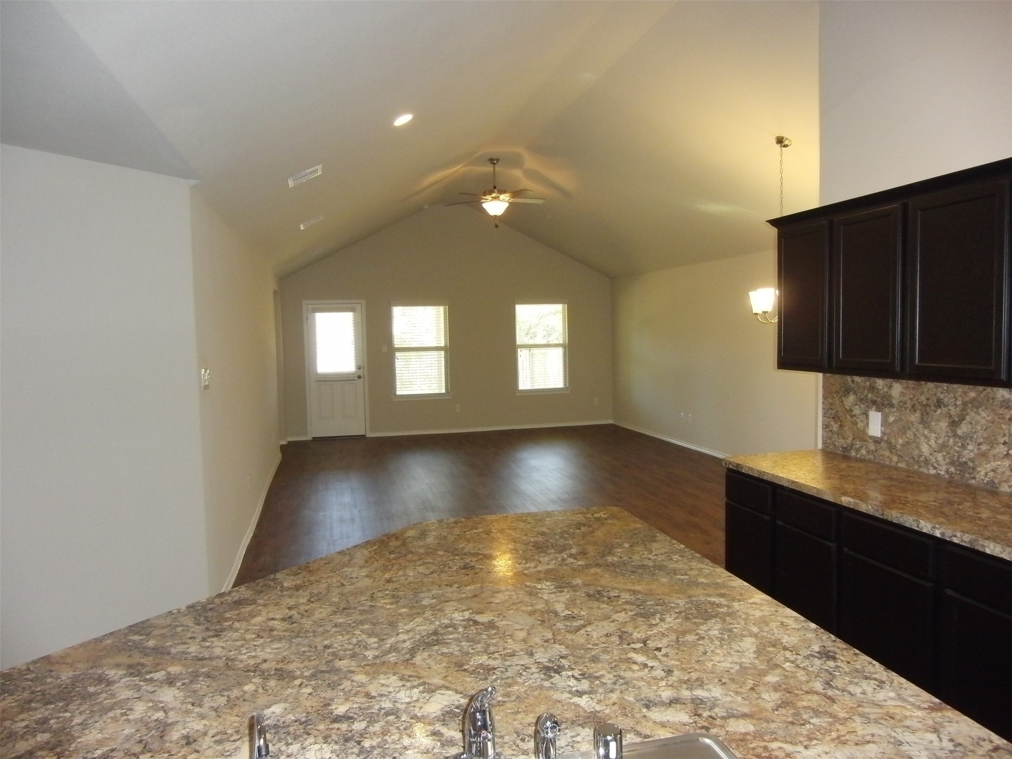 5522 Mesquite Oaks Trail Spring, TX 77389 - Photo 9 of 28 Open-concept living area with a vaulted ceiling, featuring a kitchen with dark cabinetry and granite countertops. The space has hardwood flooring and ample natural light from multiple windows and a glass door.