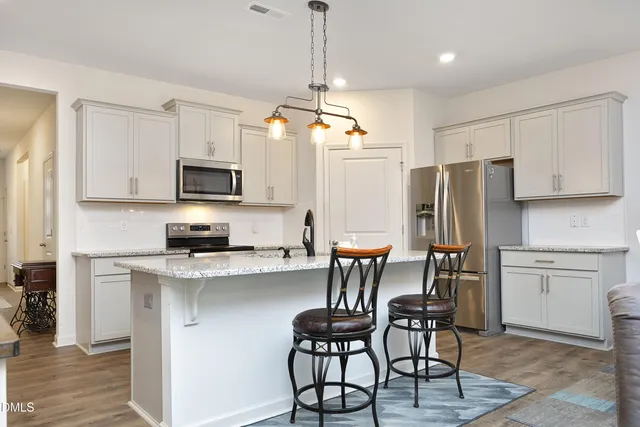 a kitchen with stainless steel appliances a dining table chairs refrigerator and microwave
