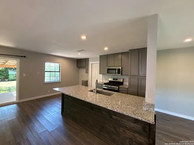 a kitchen with kitchen island granite countertop wooden floors wooden cabinets a sink and appliances