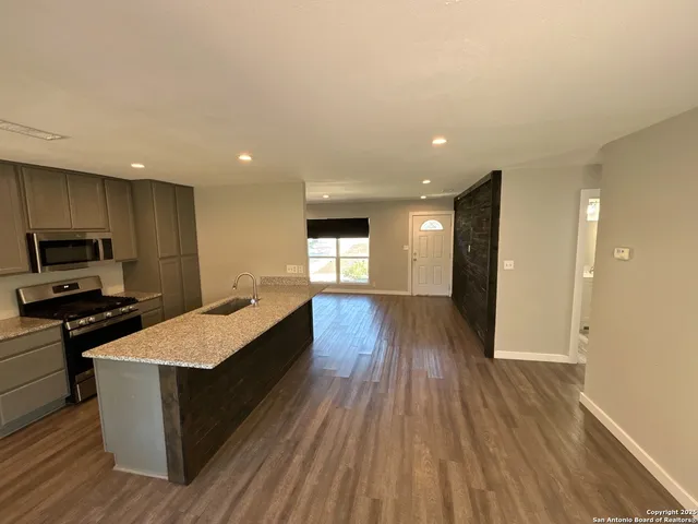 a large kitchen with stainless steel appliances granite countertop a large counter top a stove and a wooden floors