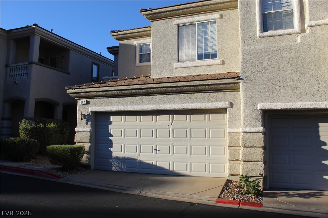 207 Priority Point Street Henderson, NV 89012 - Photo 4 of 23 Multi-level townhouse structure showcases a textured stucco facade and integrated multi-car garage storage.