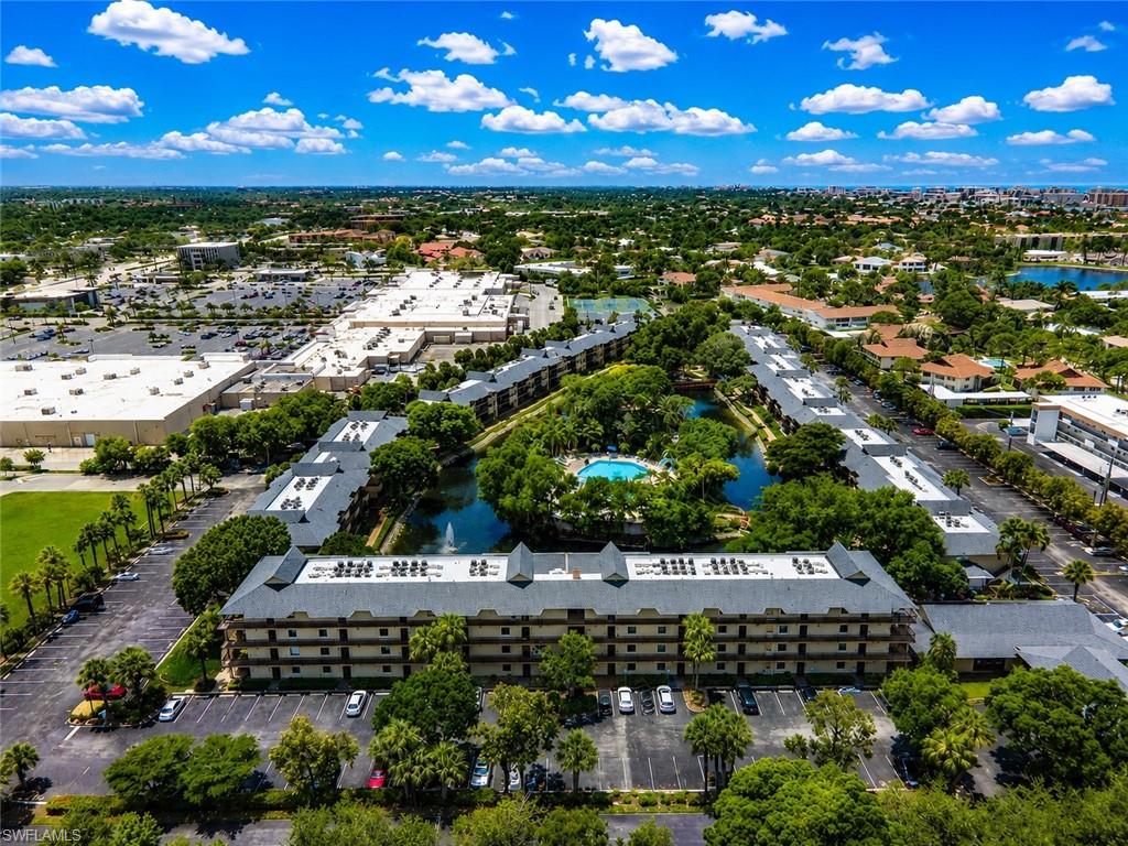 600 Neapolitan Way, Unit 449 Naples, FL 34103 - Photo 41 of 44 Aerial perspective showcasing a multi-story residential complex with a central pond and swimming pool