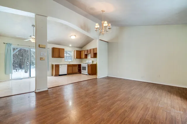 an empty room with wooden floor and kitchen view