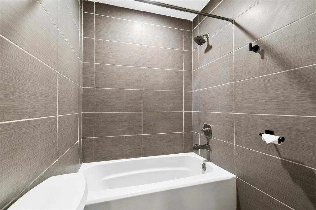 909 North Dove Road Grapevine, TX 76051 - Photo 20 of 30 Primary Bathroom featuring a white bathtub, a shower with a chrome showerhead, and gray tile walls with white grout