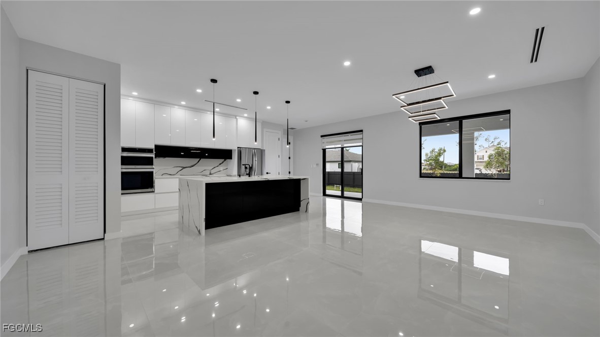 910 Northwest 36th Place Cape Coral, FL 33993 - Photo 8 of 46 a large white kitchen with kitchen island a sink wooden floor and a stove top oven