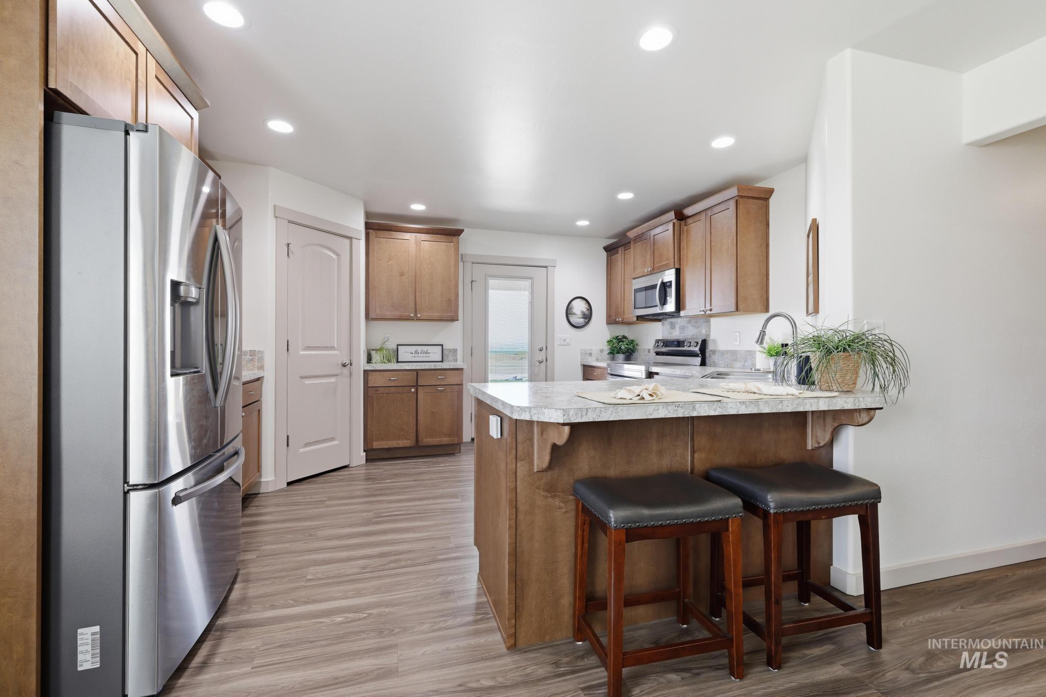 178 Syringa Loop Shoshone, ID 83352 - Photo 10 of 35 Chef's kitchen featuring stainless steel French-door refrigerator, wood cabinetry, white quartz countertops, and a large island with seating for two