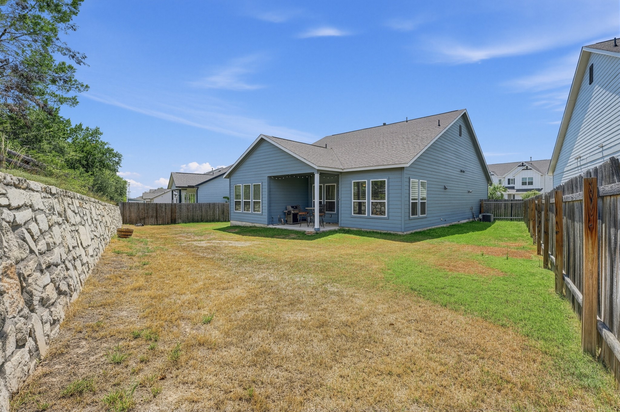 145 Brooks Ranchi Drive Kyle, TX 78640 - Photo 33 of 40 An expansive backyard features a level lawn bordered by a stone retaining wall and wooden fencing.