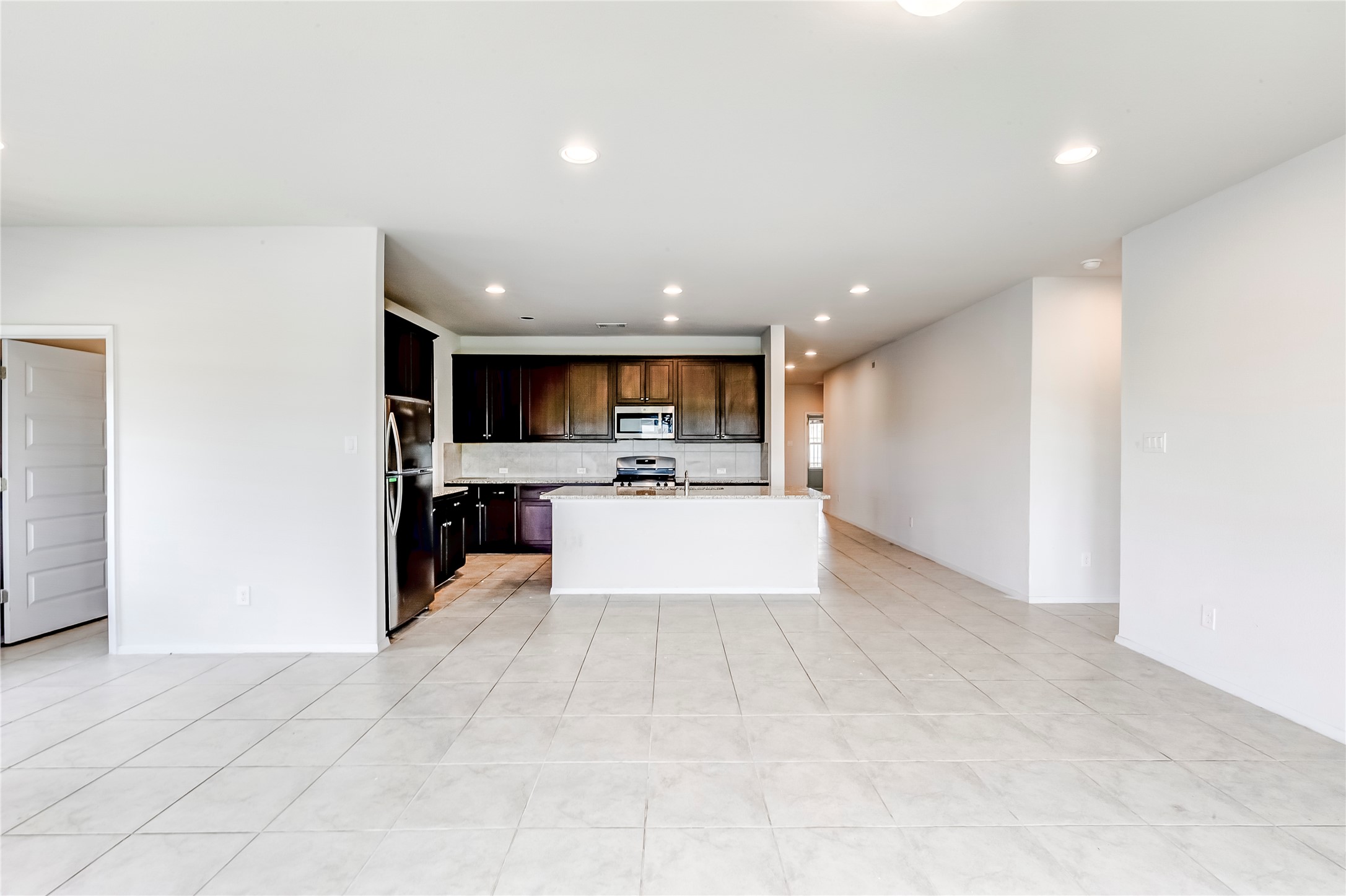 2721 Winding Creek Road Kyle, TX 78640 - Photo 8 of 27 Open-concept living area featuring light-toned tile flooring, recessed lighting, and a kitchen with dark cabinetry, stainless steel appliances, and a central island with a breakfast bar