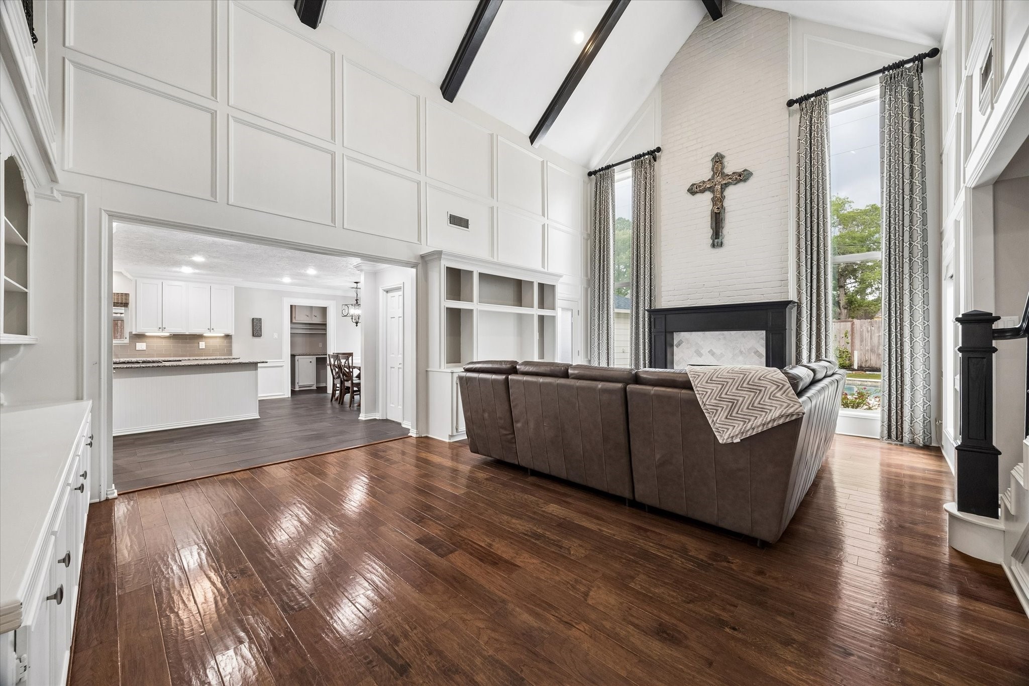 9410 Taidswood Drive Spring, TX 77379 - Photo 16 of 40 This absolutely stunning family room/great room features soaring high ceilings with beautiful beams to accentuate the cathedral style features! A floor to ceiling brick fireplace with modern updates featuring a black wooden mantle and designer tile in lay makes the perfect centerpiece to the room. Adjacent the fireplace on either side are custom drapes and curtain rods, and across from the fireplace is a wall of stunning wooden built in cabinets perfect for displaying all of your favorite things.
