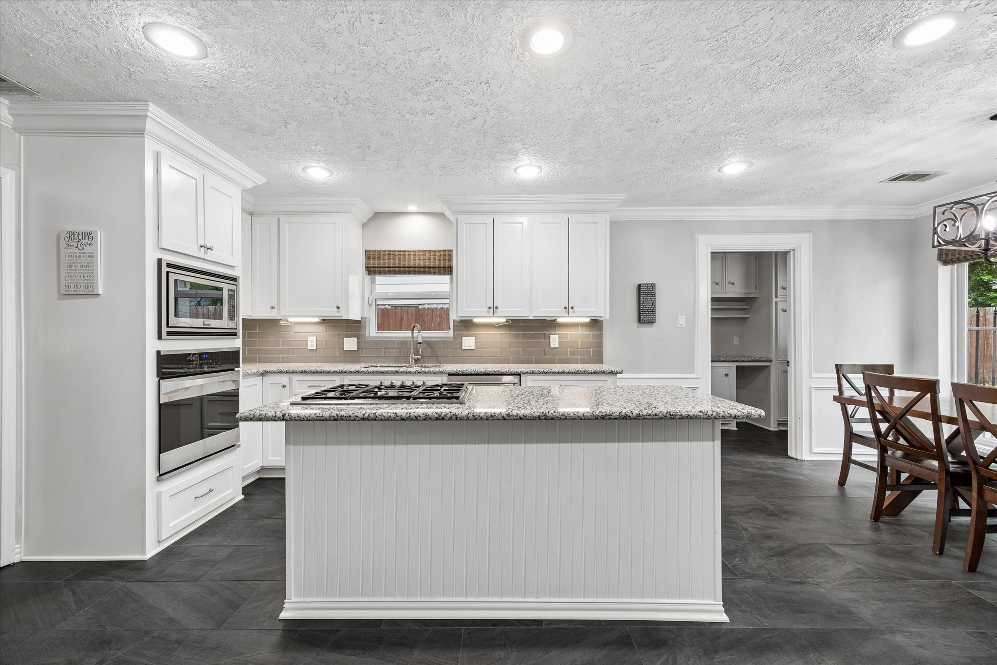 9410 Taidswood Drive Spring, TX 77379 - Photo 19 of 40 The remodeled kitchen features gorgeous tile flooring that compliments the beautiful white cabinetry. Featured here is the island with cooktop and the breakfast room/eat-in kitchen, and entrance to the mudroom and laundry room off to the right.