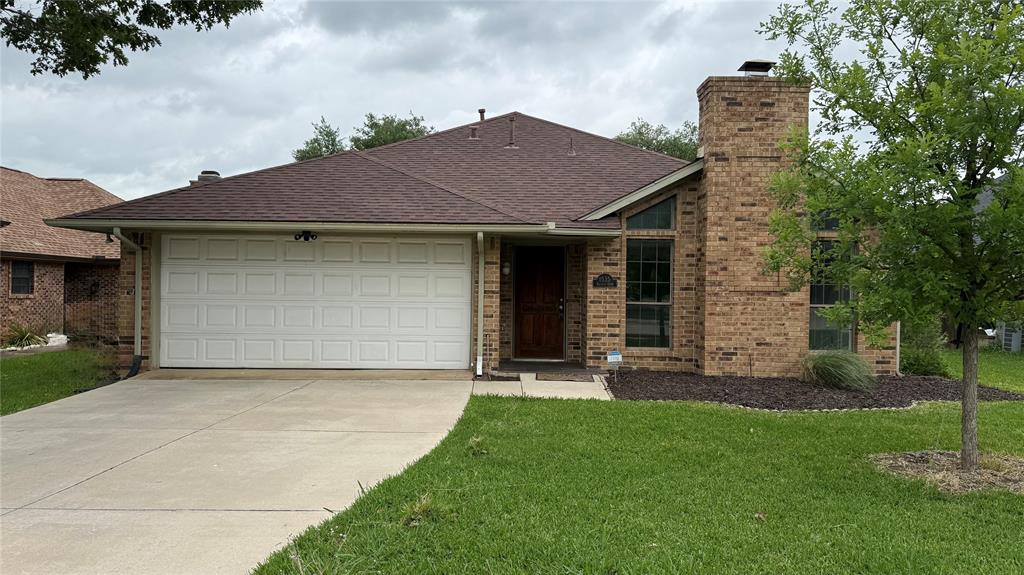 Brick exterior featuring a prominent chimney, a two-car garage with a panel door, a dark wood-finish entry door, and an asphalt shingle roof