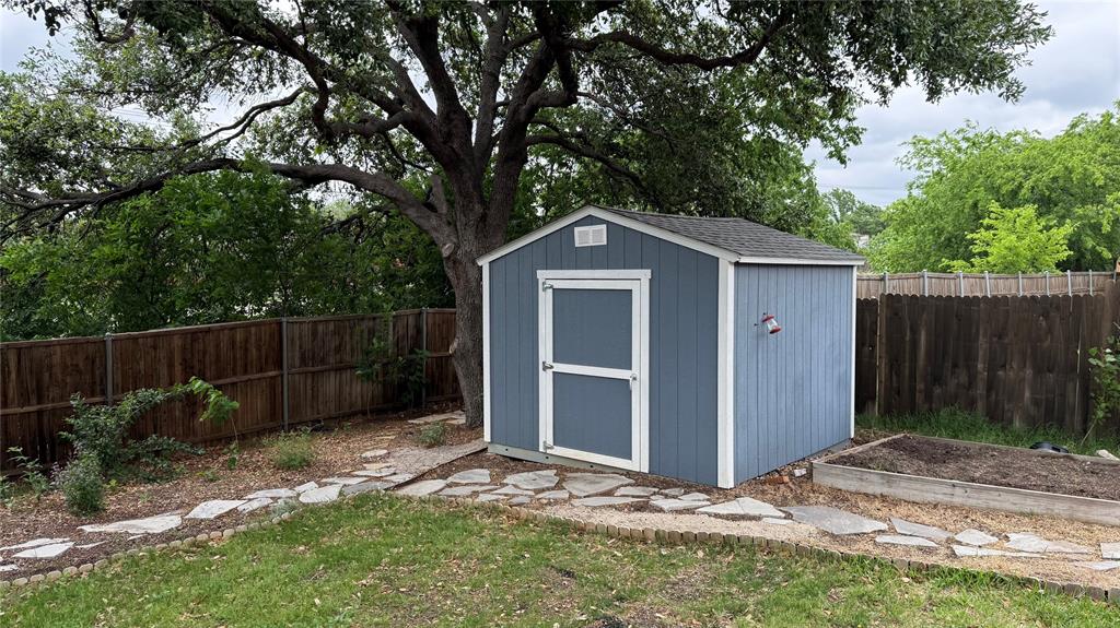 1535 Raleigh Drive Carrollton, TX 75007 - Photo 24 of 24 Backyard shed with blue siding and white trim, featuring a side garden bed, flagstone pathway, and mature trees providing natural shade