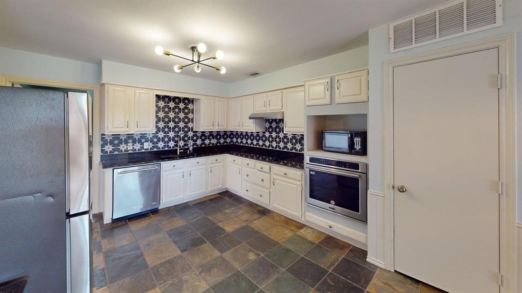 1535 Raleigh Drive Carrollton, TX 75007 - Photo 4 of 24 Kitchen featuring white cabinetry, patterned backsplash, built-in oven, stainless steel appliances, and slate-finish tile flooring